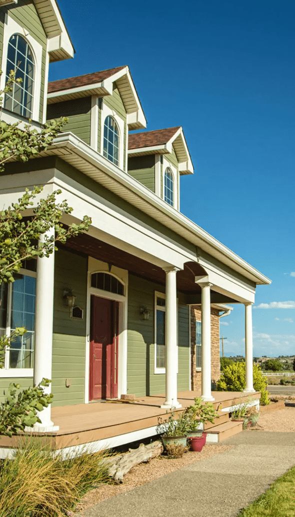Green house with porch under blue sky.
